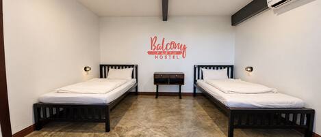 A hostel room with two beds, a small table, and a wall-mounted air conditioning unit.