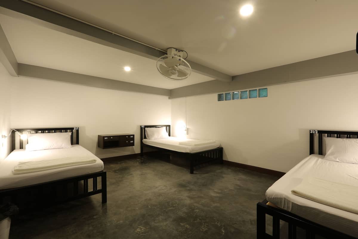 A hotel room with three single beds, a ceiling fan, recessed lighting, and a small wall-mounted shelf.
