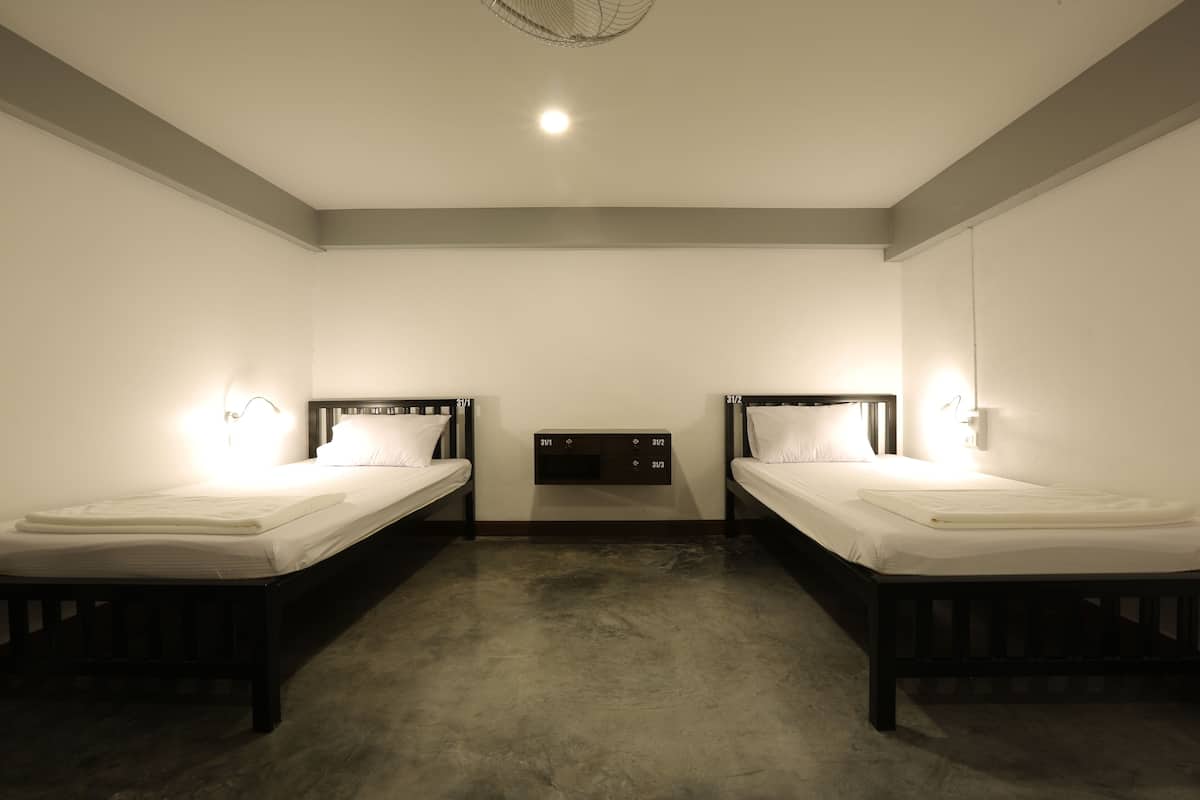 A room with two single beds, a small wall-mounted TV, and a ceiling light.