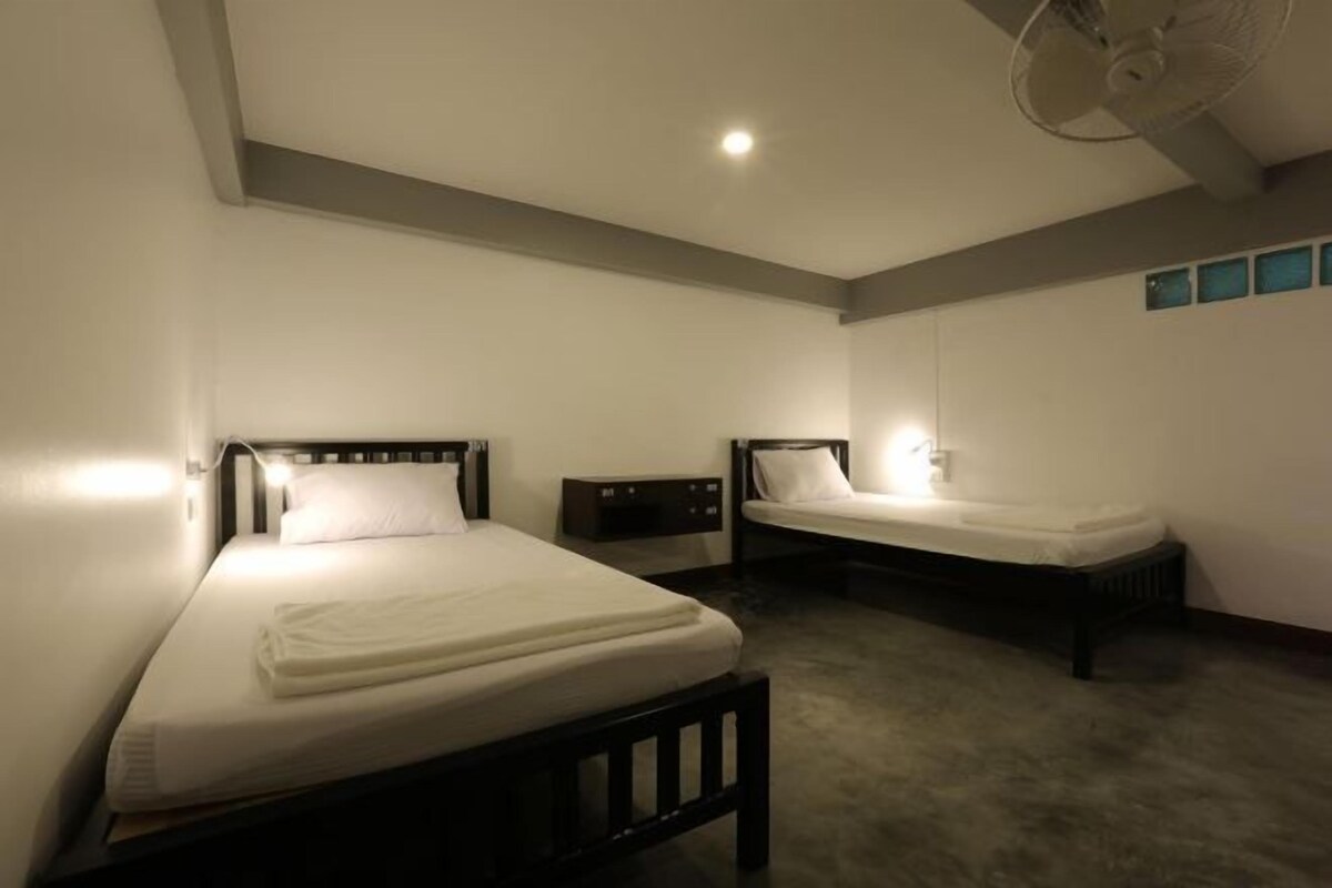 A hotel room with two single beds, a bedside table, a nightstand, and a ceiling fan.