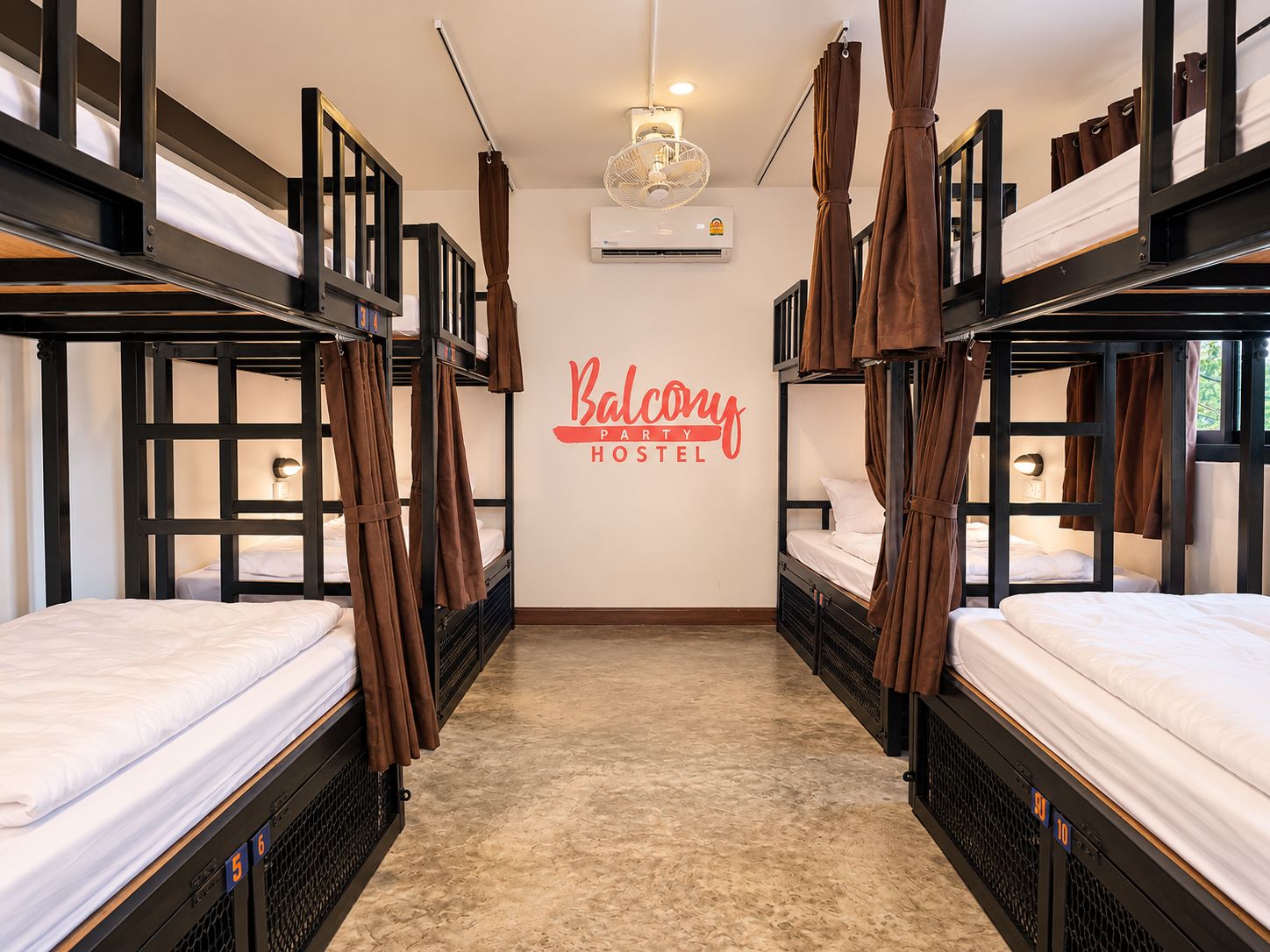 A hostel room with bunk beds, a wall-mounted air conditioner, and a sign reading 'Balcony Party Hostel'.