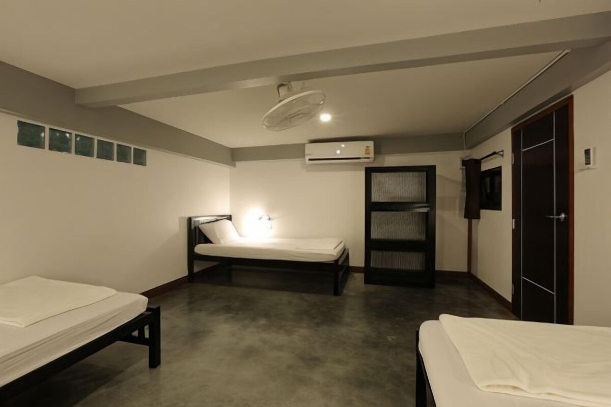 A hotel room with two single beds, a ceiling fan, an air conditioning unit, a wardrobe, and a small shelf.