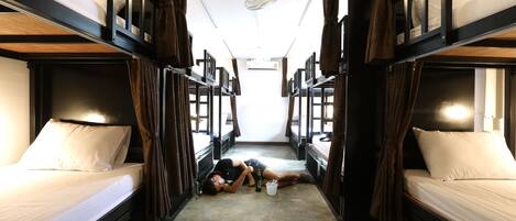Kapea käytävä, jonka molemmilla puolilla on kerrossängyt, yläpuolella tuuletin ja lattialla makaava henkilö.