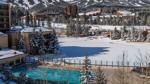 Um resort com piscina, paisagem nevada e edifícios ao fundo.