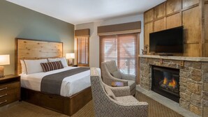 Quarto de hotel com uma cama, uma poltrona, televisão e lareira.