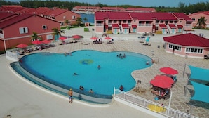 Una gran piscina rodeada de edificios con techos rojos, algunos con balcones y unas pocas palmeras.