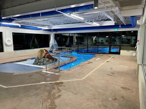 Una piscina con tobogán, paredes de vidrio y techo con vigas y luces a la vista.