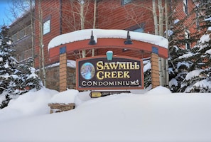 Une enseigne pour le complexe de condominiums Sawmill Creek, avec un paysage enneigé et un bâtiment rouge en arrière-plan.
