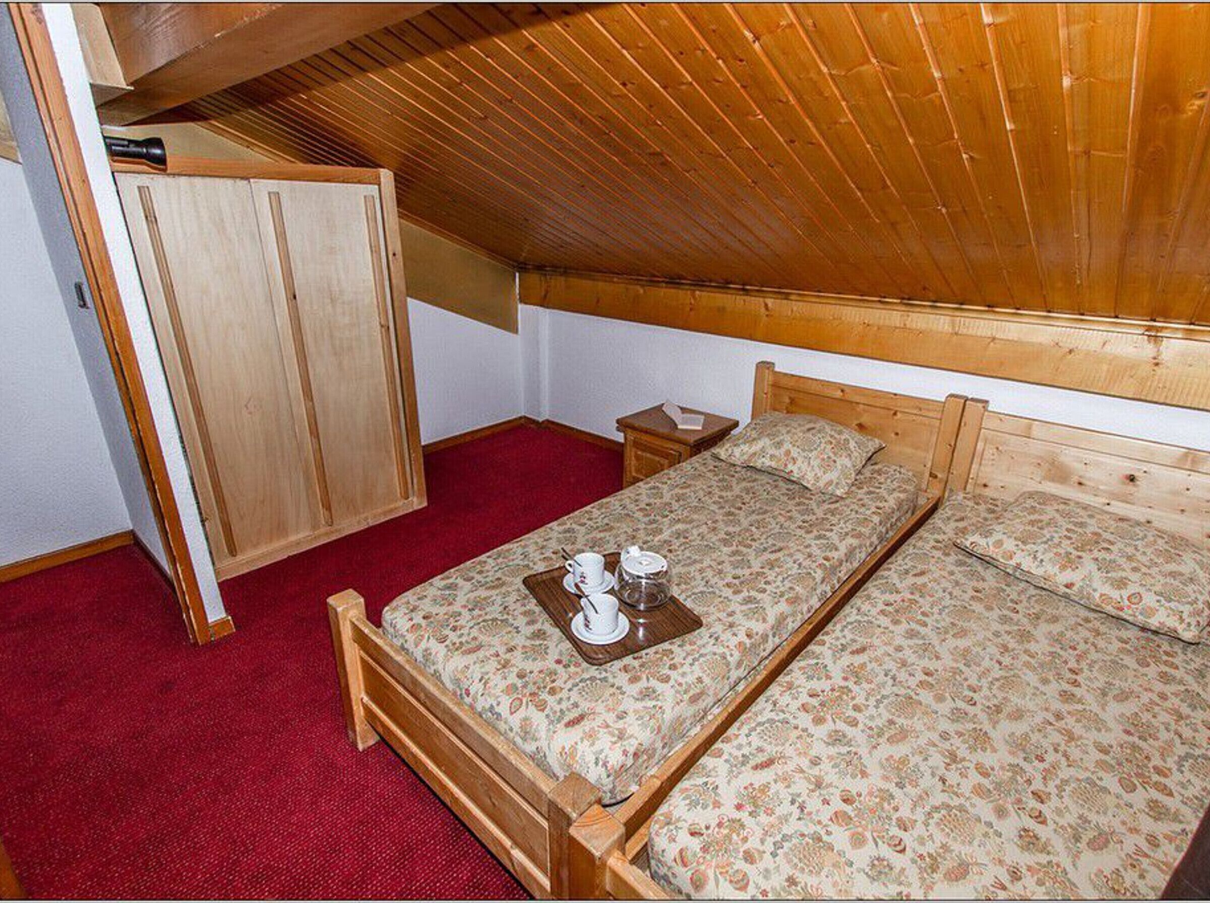 A small, cozy bedroom with a wooden ceiling, a single bed with floral bedding, a nightstand, and a wardrobe.