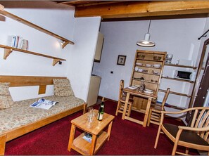 Ein gemütliches Wohnzimmer mit einer Couch, einem kleinen Holztisch, einem Esstisch mit Stühlen, einem Bücherregal und einer Mikrowelle.