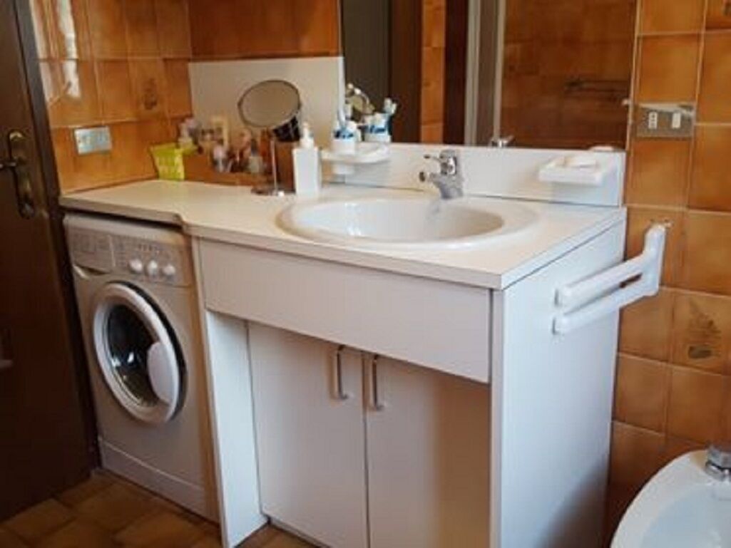 Ein kleines Badezimmer mit einem weißen Waschbecken, einem Spiegel und einer Waschmaschine.
