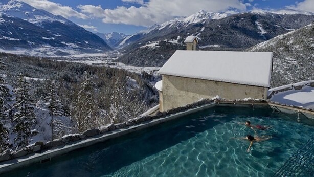 A swimming pool with clear water, surrounded by snow-covered mountains and a clear sky.
