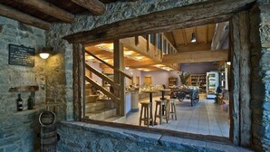 A rustic interior with stone walls, wooden beams, and a bar area with stools.