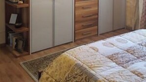 A bedroom with a bed, a wardrobe, and a shelf unit with various items.