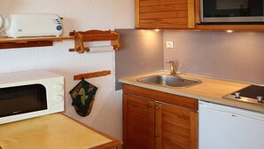 A compact kitchen with wooden cabinets, a microwave, a sink, and a wooden shelf with a toaster.