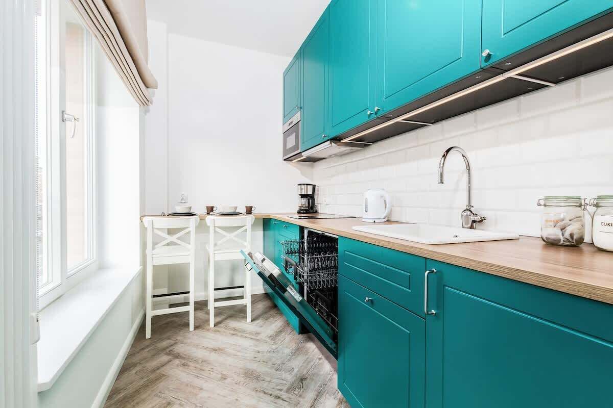 Una cocina con gabinetes color turquesa, encimeras blancas y una ventana con vistas.