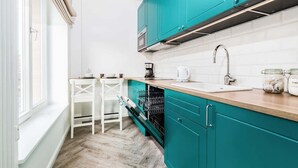 Una cucina con mobili color petrolio, ripiani bianchi e una finestra con vista.