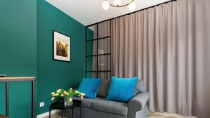 Un soggiorno moderno con pareti color acquamarina, un divano grigio con cuscini blu, un tavolino con un vaso di fiori e un'ampia finestra con tende.
