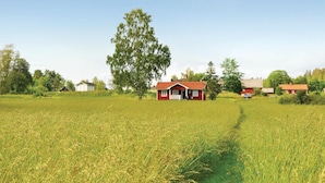 Punainen talo, jossa on kuisti, sijaitsee maaseudulla peltojen ja puiden ympäröimänä.