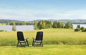 Deux chaises noires sont placées face à un lac, avec une colline boisée en arrière-plan.