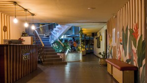 A hotel lobby with a reception desk, a staircase, and a bench.