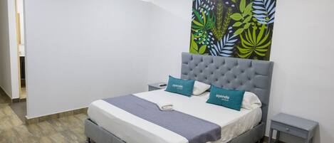 Una habitación de hotel moderna con una cama gris, dos almohadas, una mesita de noche pequeña y un cuadro abstracto grande en la pared.