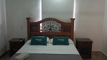 Een hotelkamer met een houten bed, twee groene kussens, een witte spreidek en een houten nachtkastje aan beide zijden.