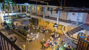 A multi-level outdoor dining area with tables and chairs, surrounded by plants and umbrellas.