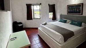 A bedroom with a bed, a desk, a chair, a window, and a painting on the wall.