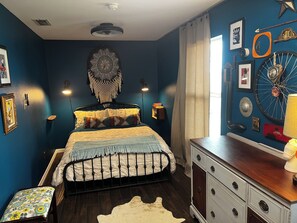 Une chambre à coucher comprenant un lit, une commode, des éléments de décoration murale et un ventilateur de plafond.