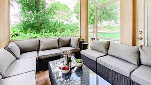 A sunroom with a large window, a sectional sofa, a glass coffee table, and a small potted plant.