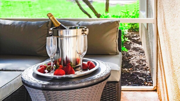 A champagne bucket with a bottle on a tray of strawberries on a wicker table by a window.