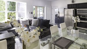 A modern kitchen with stainless steel appliances, a glass dining table, and a sofa with striped cushions.