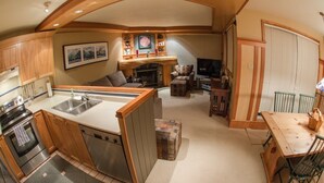 Une cuisine compacte dotée d’un îlot central, d’appareils électroménagers intégrés et d’un coin salon accueillant avec une cheminée.