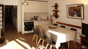A modern kitchen with white cabinets, a dining table with chairs, a built-in oven, and a pendant light.