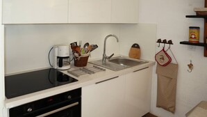 A compact kitchen with white cabinets, a black induction cooktop, a stainless steel sink, and a coffee maker.