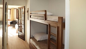 A room with two bunk beds, wooden flooring, a window with curtains, and a sofa in the background.