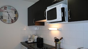 A kitchen with dark cabinets, a white microwave, a coffee maker, and a kettle on the counter. - Luxury apartment in Les Orres 1800 with pool, sauna, hammam, and WiFi (Les Orres)