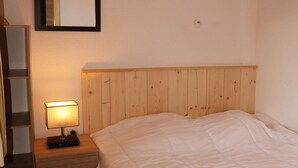A bedroom with a wooden headboard, a bedside table with a lamp, and a bed with a white duvet. - Modern 2-Room Apt for 6 with Pool, Sauna, Hammam, Near Slopes (Les Orres)