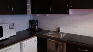 A compact kitchen with dark cabinets, a white dishwasher, a microwave, a coffee maker, and a sink. - Modern 2-Room Apt for 6 with Pool, Sauna, Hammam, Near Slopes (Les Orres)