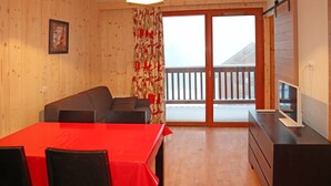 A room with a wooden interior, a red table, two chairs, a sofa, a TV, and a balcony with a railing. - Modern 2-Room Apt for 6 with Pool, Sauna, Hammam, Near Slopes (Les Orres)
