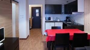 A compact kitchen with a microwave, toaster, and sink. There is a dining area with a red table and black chairs. - Modern 2-Room Apt for 6 with Pool, Sauna, Hammam, Near Slopes (Les Orres)