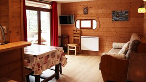 A cozy cabin interior with a wooden interior, a dining table with a tablecloth, a sofa, a TV mounted on the wall, and a window with curtains. - Ski-in/ski-out apartment for 6, balcony, near daycare (Les Orres)
