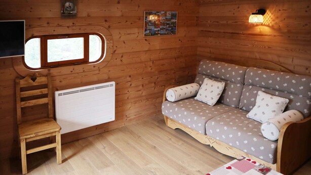 A cozy wooden room with a sofa, a small table, and a radiator. - Ski-in/ski-out apartment for 6, balcony, near daycare (Les Orres)