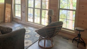A wooden cabin interior with large windows, a rocking chair, and a small table.