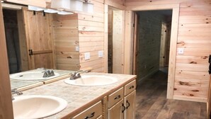 A wooden bathroom with two sinks, a mirror, and a walk-in shower.