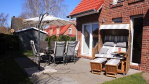 Een terras met buitenmeubilair, een overdekte tafel en een huis met rieten dak en bakstenen gevel.