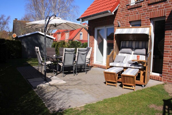 Eine Terrasse mit Gartenmöbeln, einem überdachten Tisch und einem Ziegelhaus mit rotem Dach.