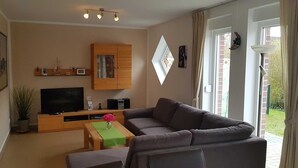 Een woonkamer met een bank, een televisie, een houten kast en een raam met gordijnen.