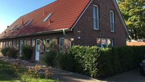 Een tweelaags bakstenen huis met een rode pannendak, meerdere ramen en een verzorgde tuin.